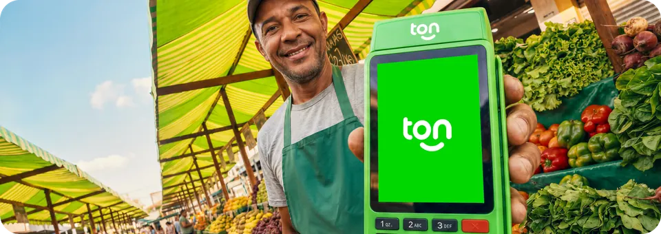 Feirante na banca de frutas e verduras mostrando a maquininha Ton
